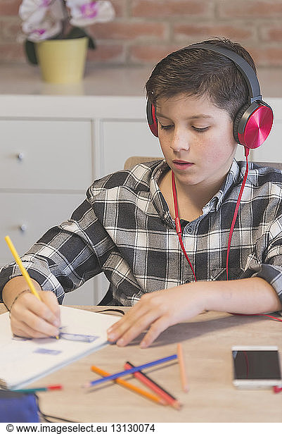 Boy listening music while coloring on book with colored pencil at table in home