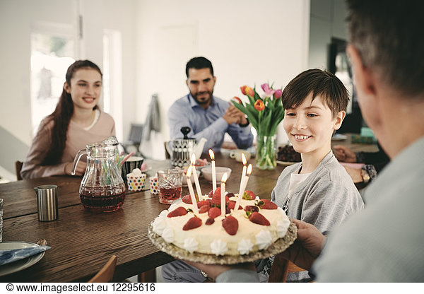 Boy looking at birthday cake while sitting with family at home