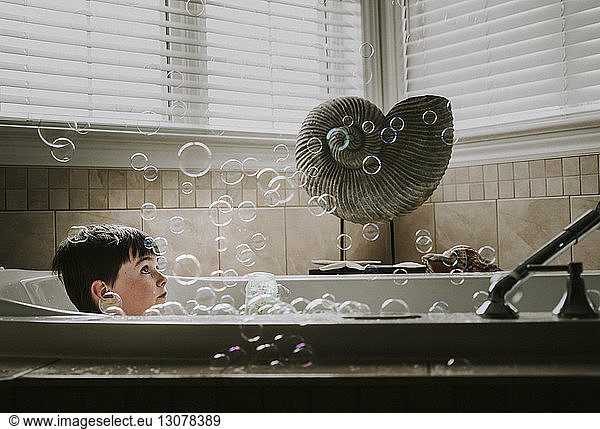 Boy looking at bubbles while taking bath in bathtub