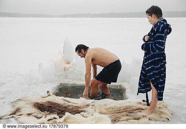 Boy looking at father taking ice bath at frozen lake