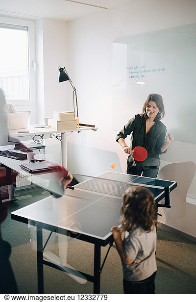 Boy looking at female professionals playing table tennis in creative office