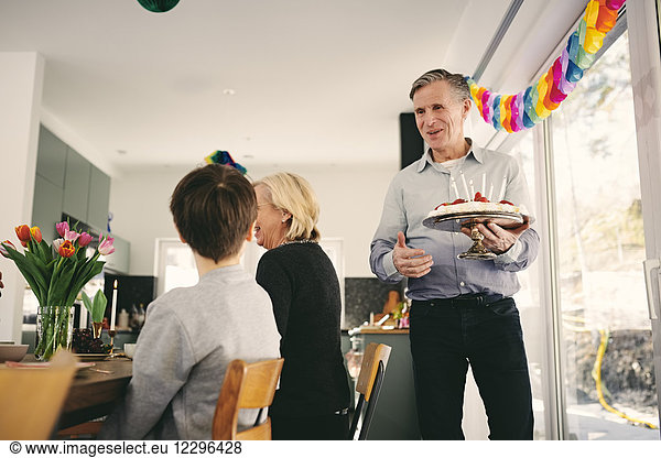 Boy looking at grandfather holding birthday cake in party