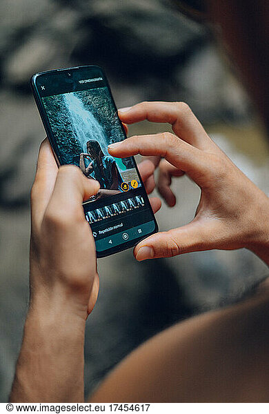 boy looking at photos taken with his cell phone in a waterfalls