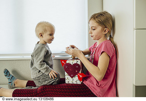 Boy looking at sister making artwork while sitting by window