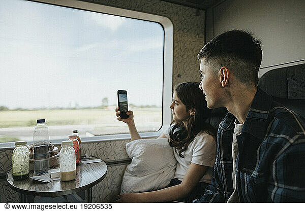 Boy looking at sister photographing through smart phone in train