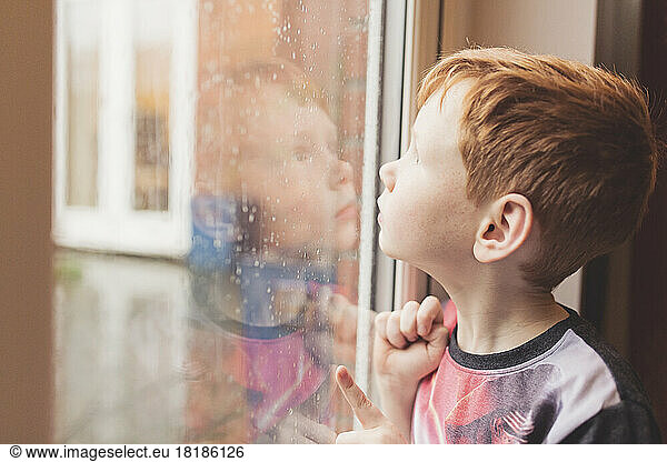 Boy looking at the rain on windowpane