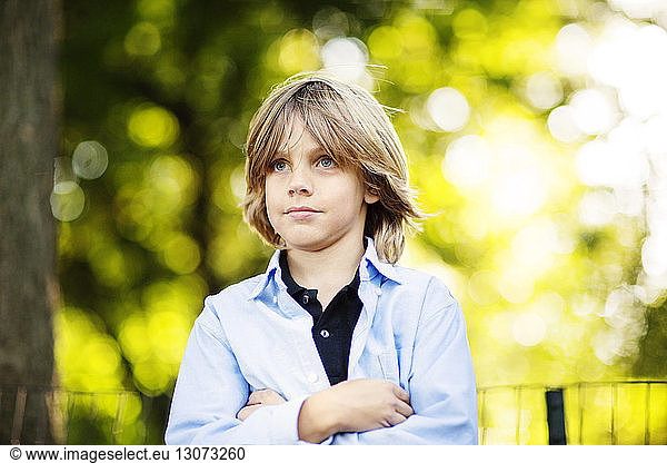 Boy looking away while standing with arms crossed at park