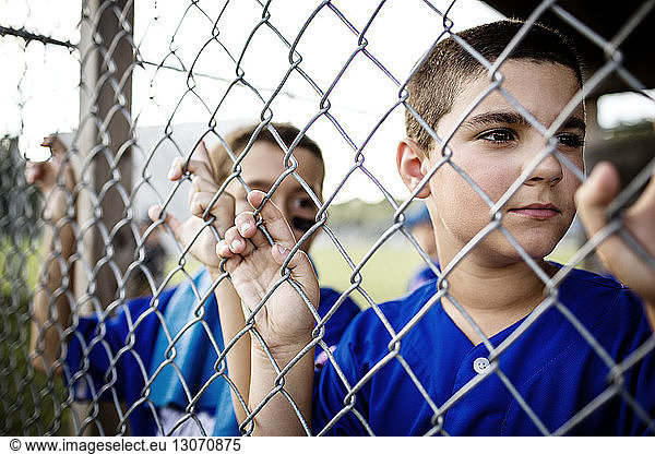 Boy looking through fence while standing in dugout
