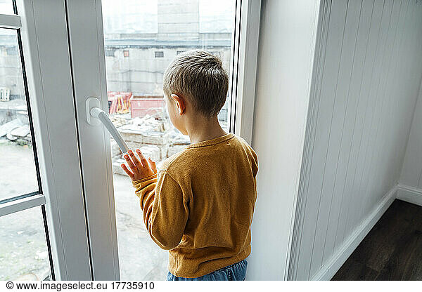Boy looking through glass window at home