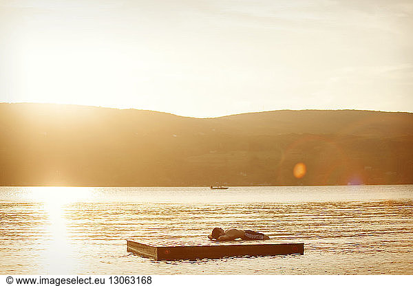 Boy lying on floating platform in lake during sunset