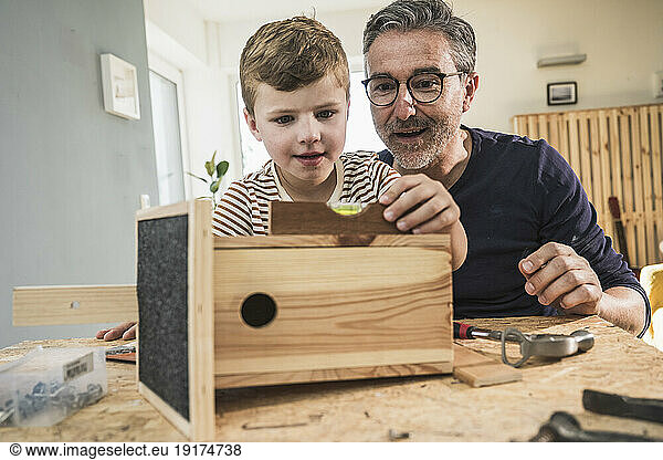 Boy making birdhouse with grandfather in living room