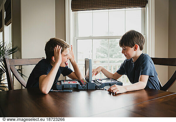 Boy making faces at his brother as they play a board game together.