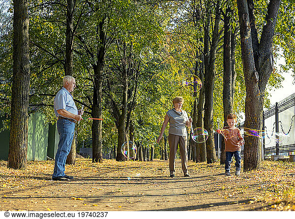 Boy making soap bubbles with grandparents in park on sunny day