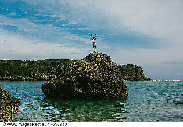 Boy on top of ocean rock formation in blue sky summer