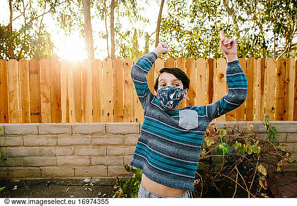 Boy Outside Wearing A Cloth Face Mask Lifts His Arms Up Exposing Belly