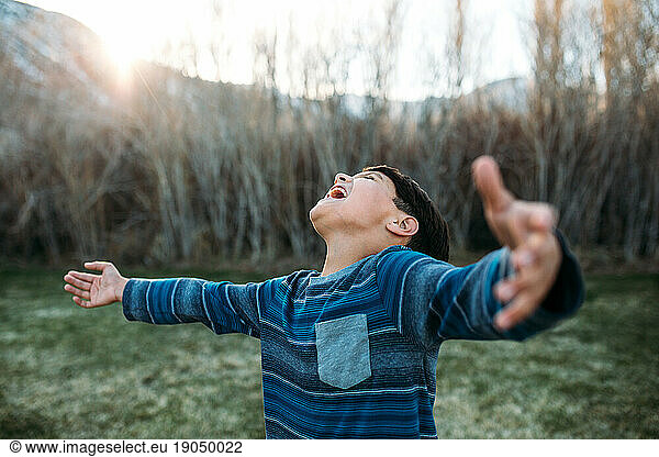 Boy outside with arms wide joyfully yells toward the sky