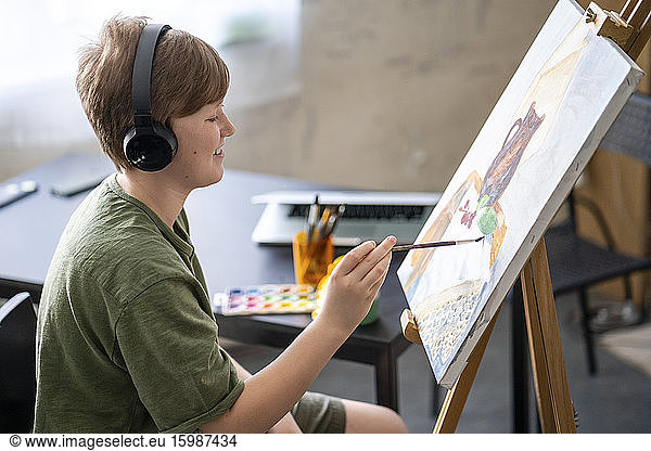 Boy painting at easel and listening to music