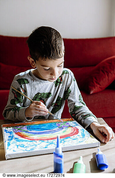 Boy painting at table in living room during summer vacation
