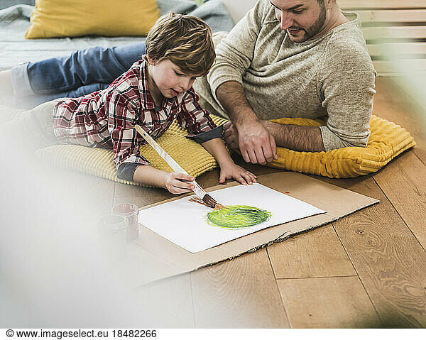 Boy painting by father lying at home