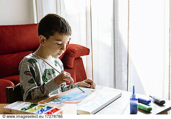 Boy painting over table at home during summer vacation