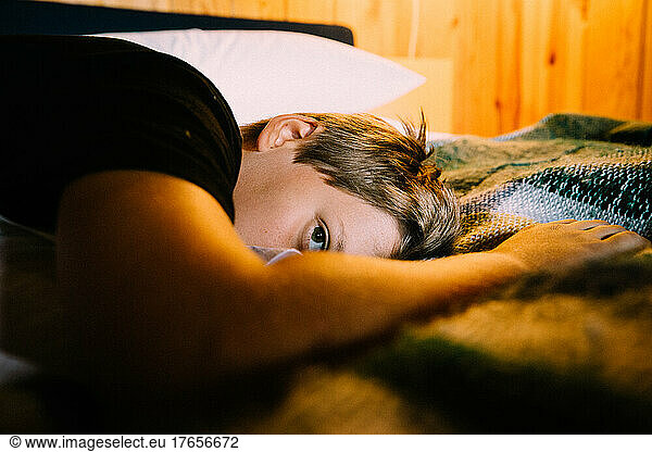 Boy Peeks from a Cozy Cabin Bed by Lamplight