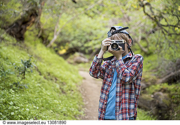 Boy photographing while standing in forest