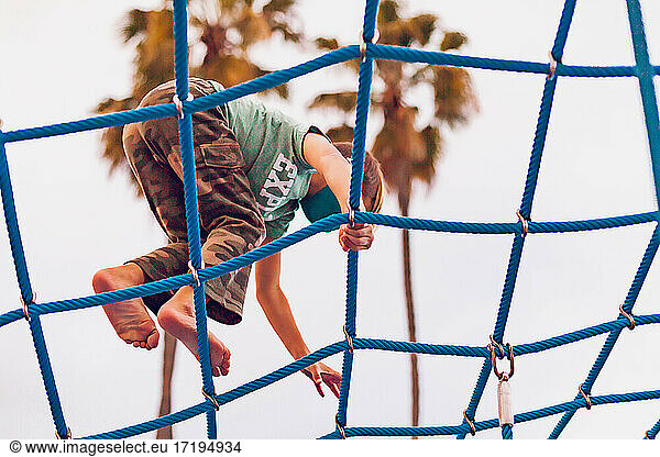 Boy playing alone at a playground - climbing on net