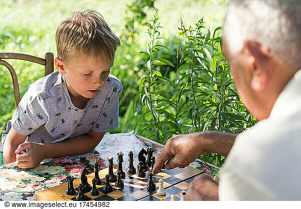 boy playing chess with her grandfather in the garden