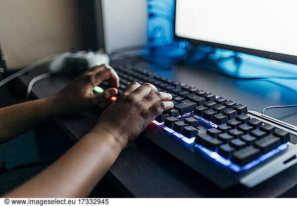 Boy playing game on computer through illuminated keyboard at home