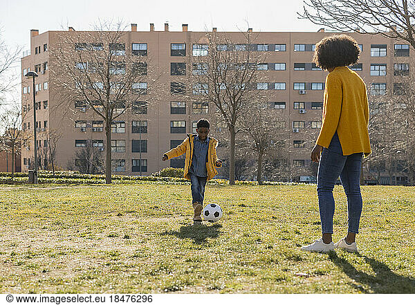 Boy playing soccer with mother in park on sunny day