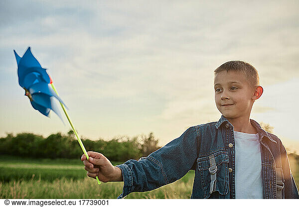Boy playing with blue pinwheel toy in agricultural field