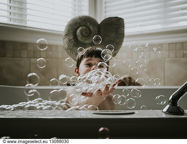 Boy playing with bubbles while taking bath in bathtub