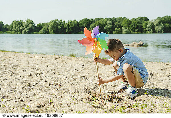 Boy playing with colorful rainbow pinwheel toy at lakeshore