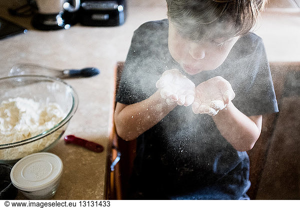 Boy playing with flour while sitting by kitchen counter