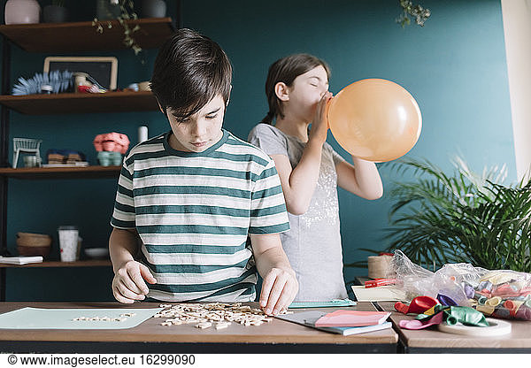 Boy playing with letters while sister blowing balloon at home