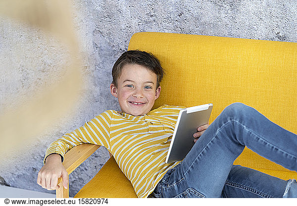 Boy playing with tablet on yellow couch