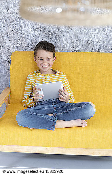 Boy playing with tablet on yellow couch