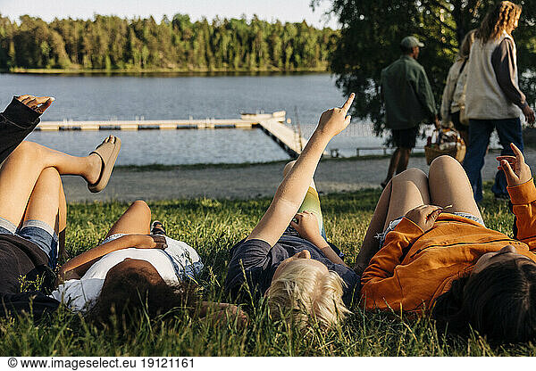 Boy pointing while lying down with friends on grass at summer camp