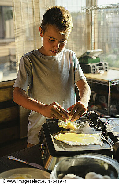 Boy preparing fried egg in kitchen at home