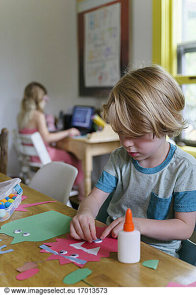 Boy (4-5) preparing paper cutout  girl (6-7) in background