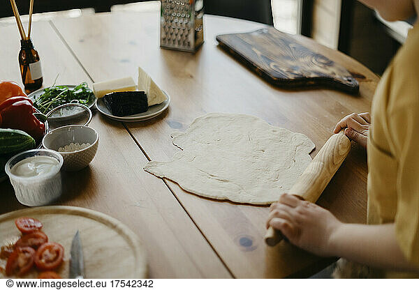 Boy preparing pizza dough with rolling pin on table