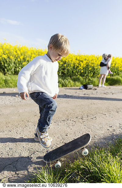 Boy preparing to skateboard on dirt road at rapeseed field