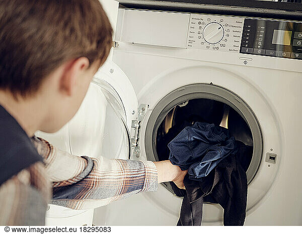 Boy putting laundry into washing machine at home