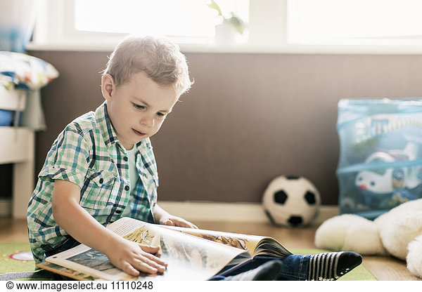 Boy reading book while sitting on floor at home