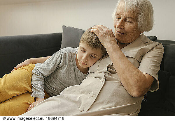 Boy relaxing by grandmother sitting on sofa at home