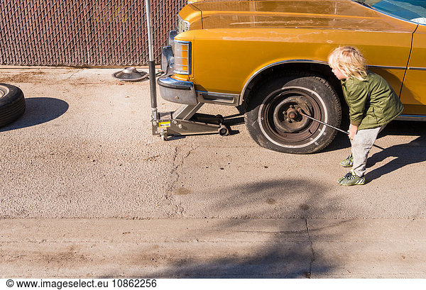 Boy removing wheel nuts from flat tyre