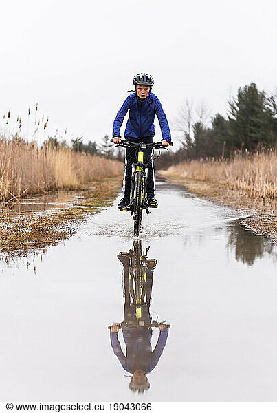 Boy riding his mountain bike through a puddle on a flooded trail.
