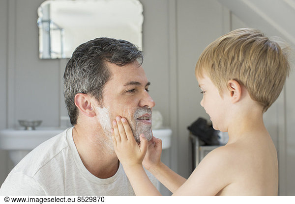 Boy rubbing shaving cream on father's face