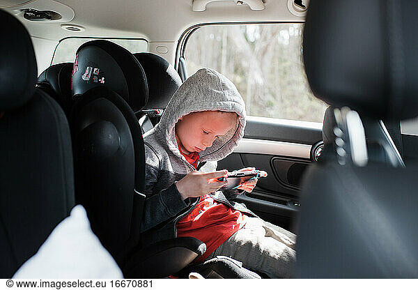 boy sat in his car seat playing a Nintendo video game console