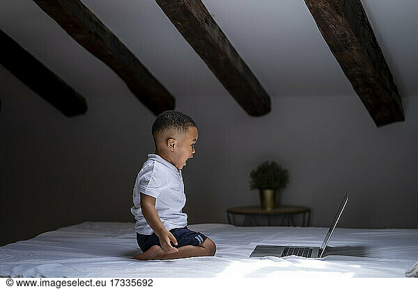 Boy screaming while looking at laptop on bed at home